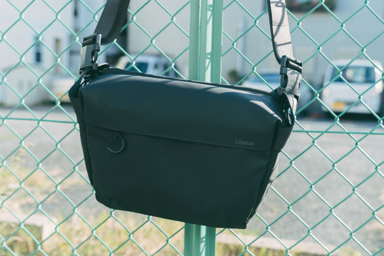 Black Ulanzi shoulder camera bag hanging on a chain-link fence outdoors