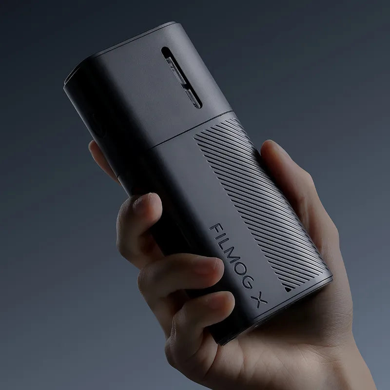 A hand holding a sleek FILMOG X portable fog machine against a dark background.