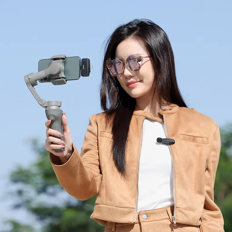 Woman using Ulanzi V6 wireless lavalier microphone with gimbal for video recording, outdoor.