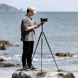 Ulanzi F38 Quick Release Video Travel Tripod in use on a rocky shoreline with a person filming.