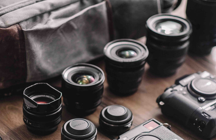 Camera lenses, two mirrorless bodies and a padded camera bag laid out on a table before a flight