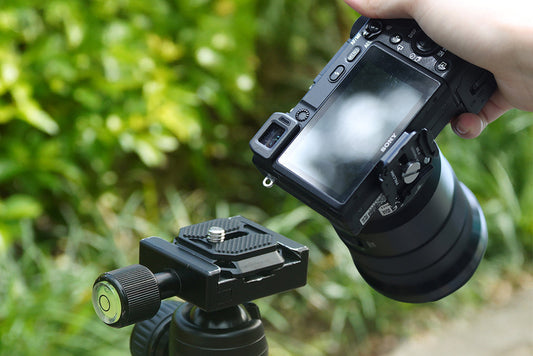 A photographer removing a camera from a tripod quick release mount outdoors