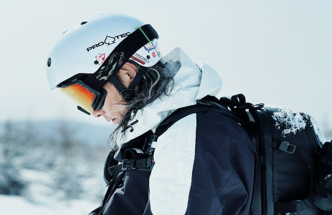 Skier in a helmet and goggles carrying a black Ulanzi camera backpack on a snowy slope