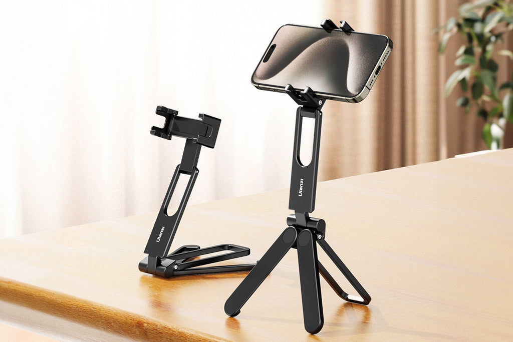 A smartphone mounted on a small black tripod standing on a wooden table next to a folded tripod.