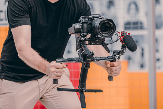 A videographer holding a professional camera rig with dual handles and an attached microphone, preparing for smooth camera movement.