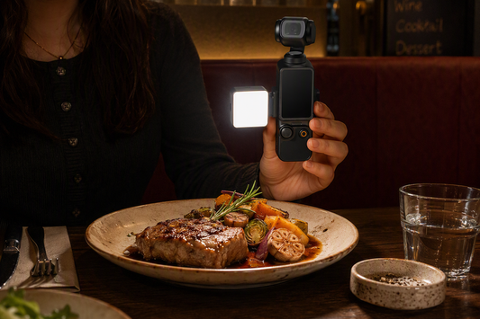 A small magnetic pocket LED light held beside a plated dish in a dim restaurant booth, creating soft side light across the food.