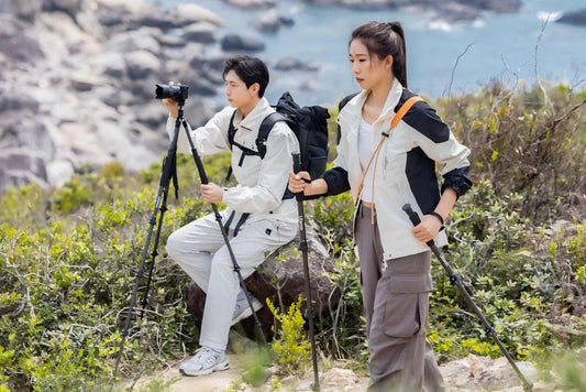 A man capturing the coastal view with a camera on a tripod while a woman hikes along the rocky path.