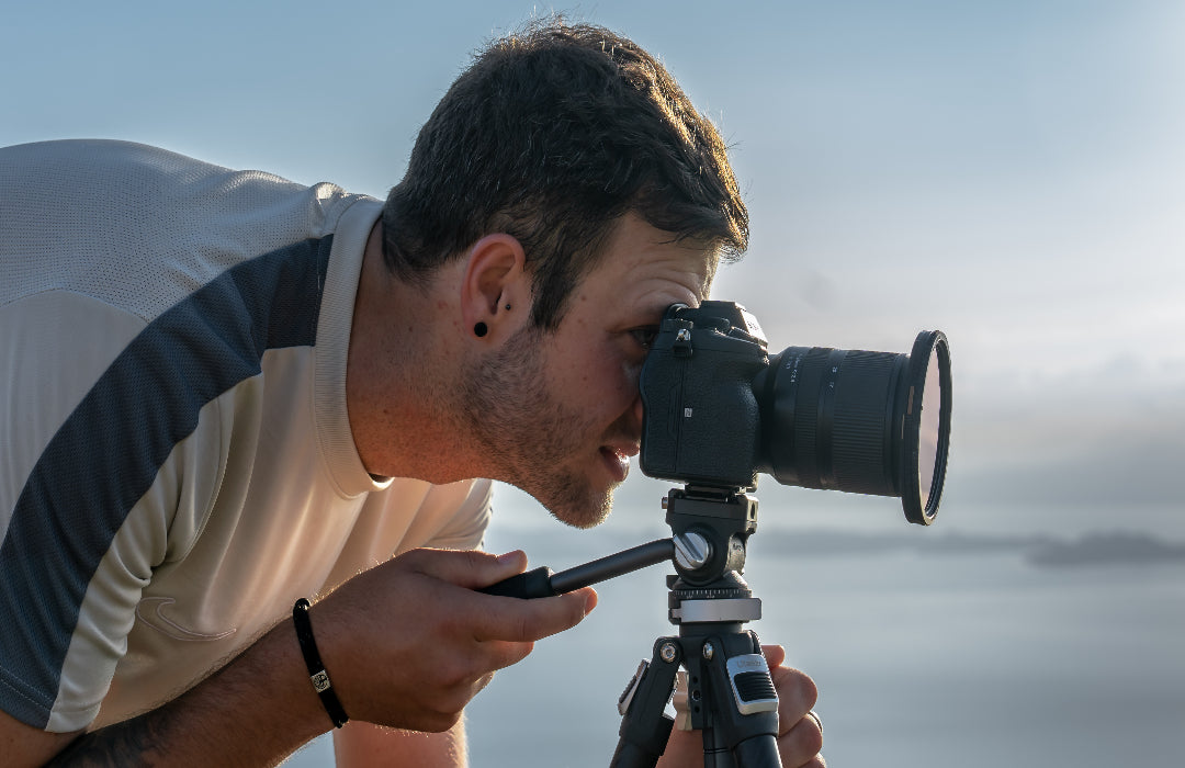 A photographer looking through the viewfinder of a camera mounted on a tripod