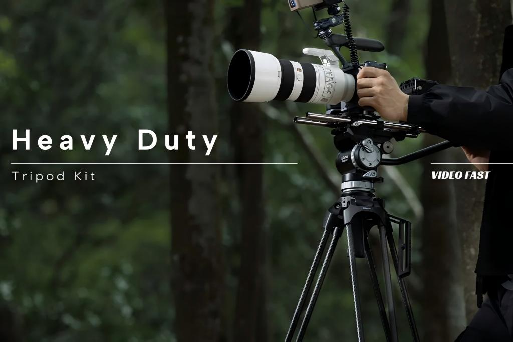 A person holding a camera with a large telephoto lens mounted on a heavy-duty tripod kit outdoors.