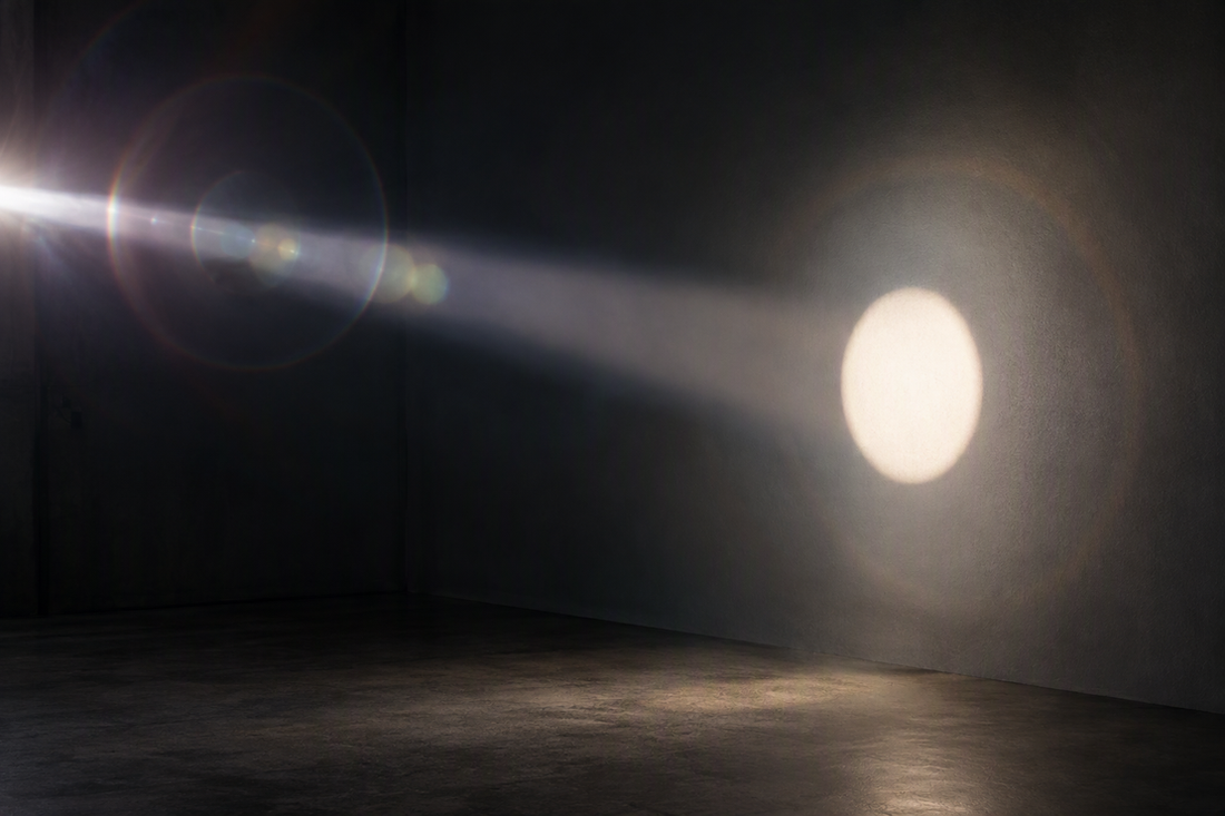 A narrow beam projects a clean circular spot while stray flare and light spill spread across a dark studio wall.