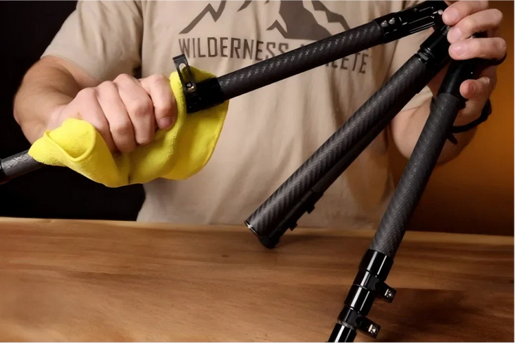A person cleaning the carbon fiber leg of a tripod with a yellow cloth.