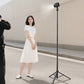 A photographer taking a picture of a woman posing, illuminated by a light on a stand.