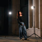 Dramatic nighttime portrait with dual LED video lights creating striking shadows and highlights against stone columns.