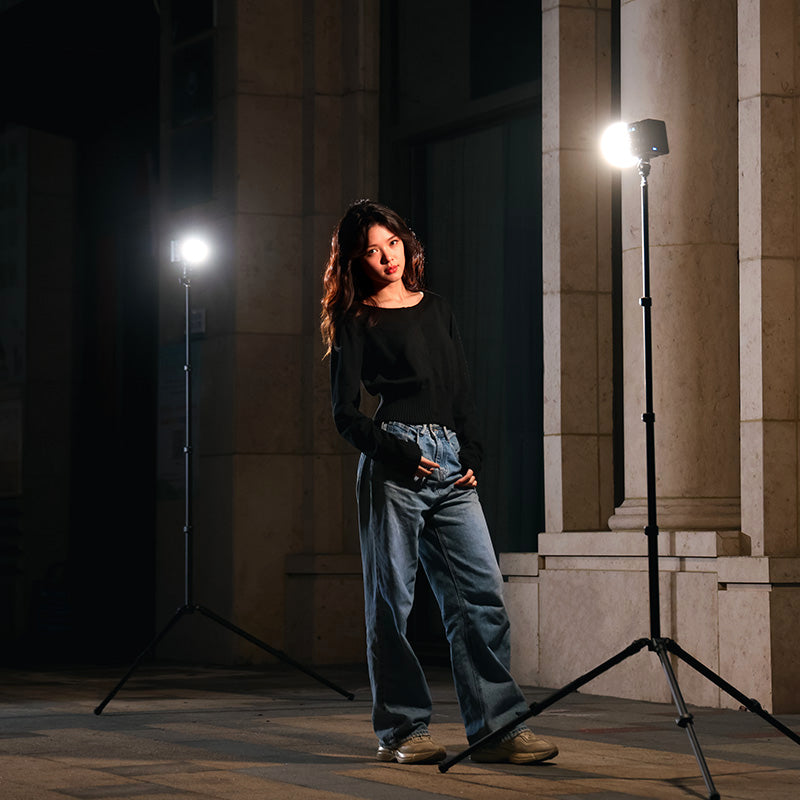Dramatic nighttime portrait with dual LED video lights creating striking shadows and highlights against stone columns.