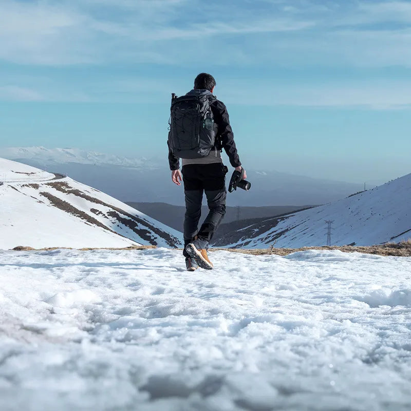 Photographer exploring snowy mountain terrain with Ulanzi camera backpack.