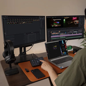 A person using a U-STUDIO stream controller with dual monitors and a laptop for video editing and content creation.