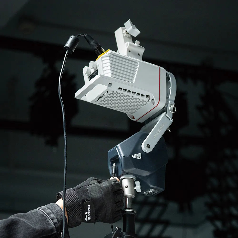 A FALCAM MOVE LED light mounted on a stand, adjusted by a gloved hand, showcasing remote-controlled lighting functionality.