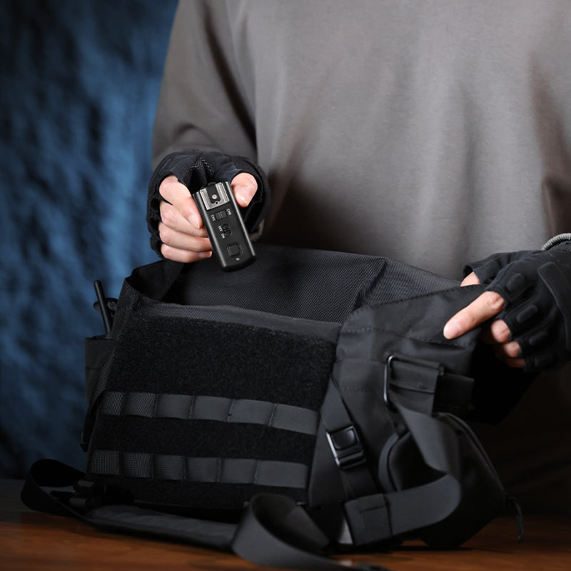 Person holding Ulanzi TT01 Wireless Flash Trigger near camera bag.