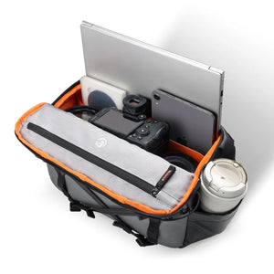 Crossbody bag packed with laptop, tablet, camera, lenses, and cup.