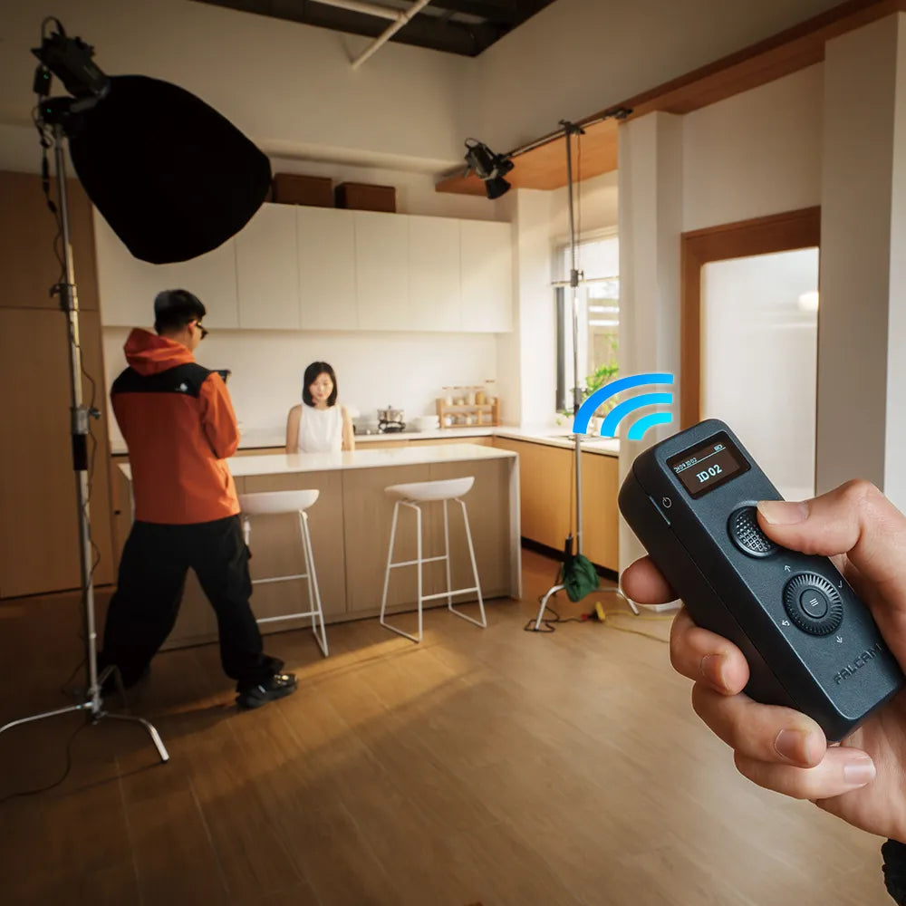 A kitchen studio setup with filming equipment and a FALCAM remote control in hand.