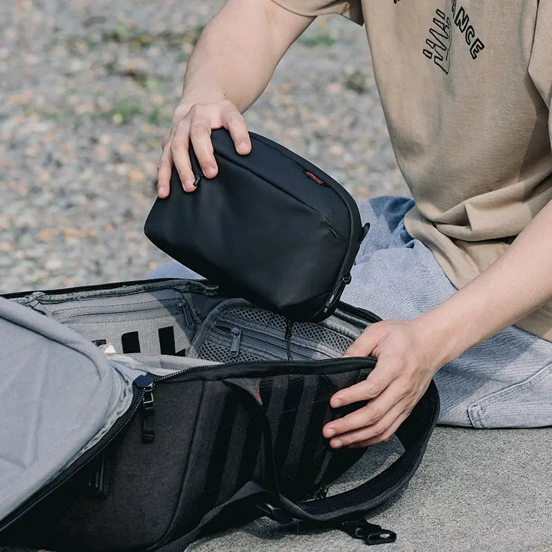 Placing black camera accessory bag into Ulanzi BP10 Backpack for outdoor photography.