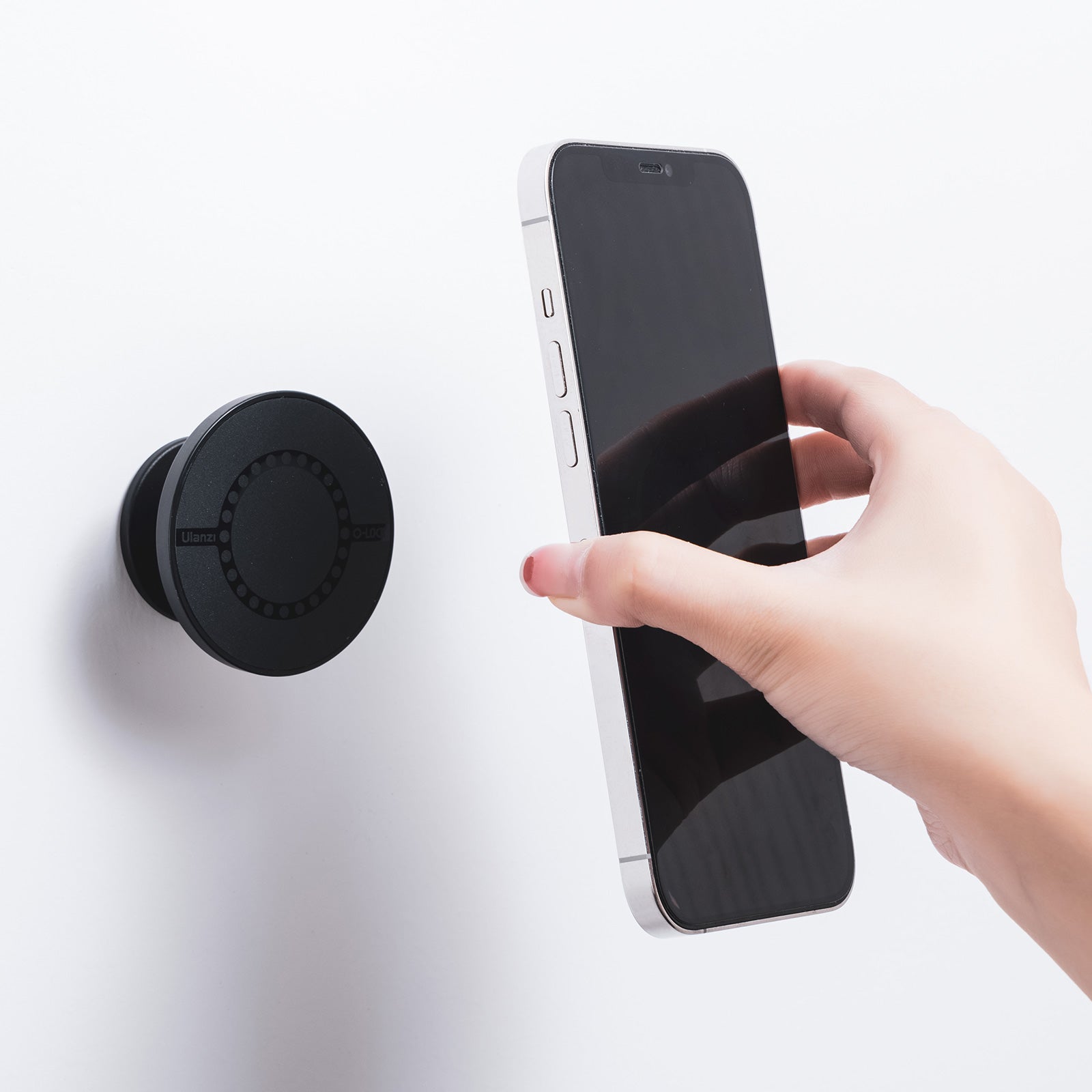 Hand positioning smartphone near Ulanzi O-LOCK magnetic sticker on wall.