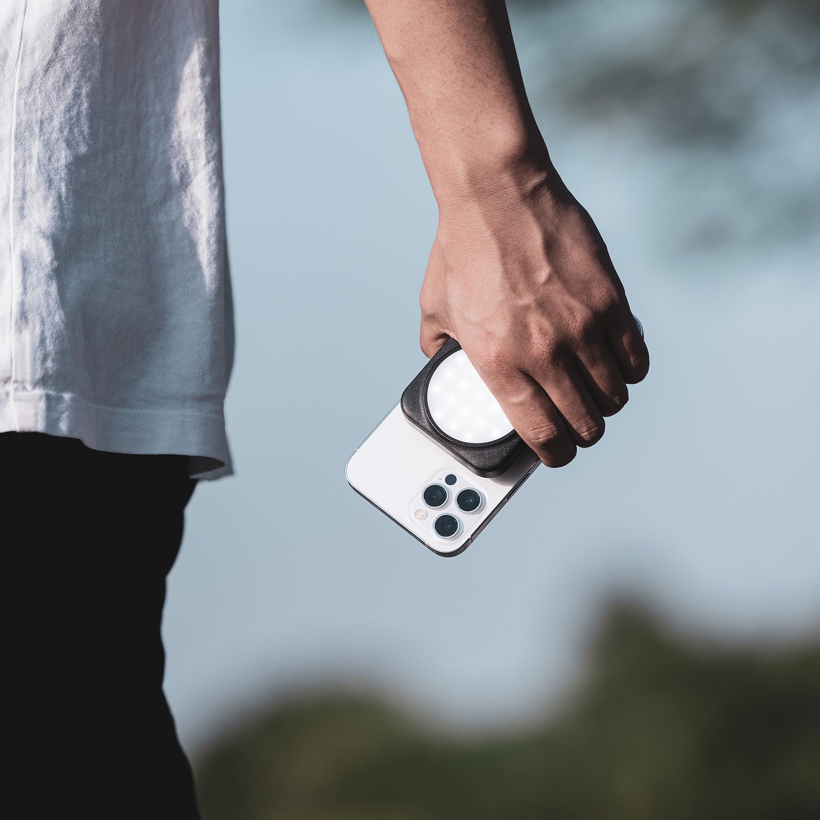 Smartphone with Ulanzi O-LOCK sticker and LED light held by a person outdoors.
